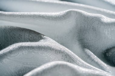 Zarif bir şekilde örtülmüş gümüş kumaşın detaylı bir görüntüsü. Yumuşak ışıkla aydınlatılmış karmaşık tasarımlar ve dokular sergileniyor. Makro