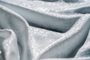 Zarif bir şekilde örtülmüş gümüş kumaşın detaylı bir görüntüsü. Yumuşak ışıkla aydınlatılmış karmaşık tasarımlar ve dokular sergileniyor. Makro