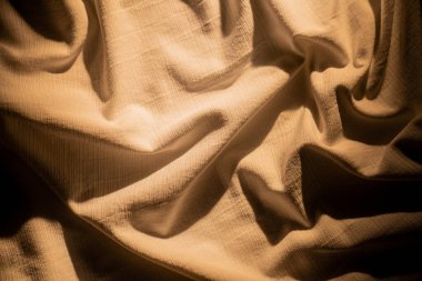 Bir bej kumaş, ışık ve gölge oyunuyla zengin dokular sergiliyor, zarif bir görünüm yaratıyor. Makro