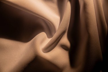 Yumuşak, akışkan bej kumaşın soyut görüntüsü dokusunu vurguluyor ve sıcak ışıkta zarifçe katlanıyor. Makro