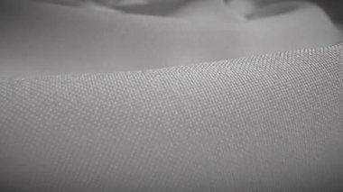 Dokuları ve yumuşak kıvrımları gösteren, karmaşık dokuma detaylarını vurgulayan beyaz bir kumaş. Makro