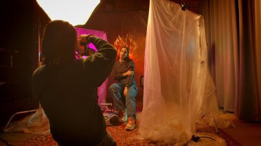 Sahne arkasında. Bir fotoğrafçı yaratıcı bir şekilde aydınlatılmış bir stüdyo ortamında canlı ve sanatsal bir portre yaratarak bir model yakalar..