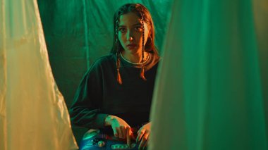 Yaratıcı ışıklandırmada bir kadın elektronik bir cihaz tutuyor, karamsar ve sanatsal bir atmosfer yaratıyor..