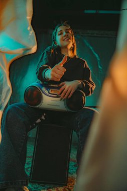 Neşeli genç bir kadın klasik bir müzik kutusuyla oturur, başparmağını kaldırır, atmosferik ışıklandırmayla çevrilidir..