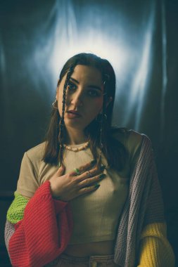 Çok renkli bir süveter giyen bir kadın, yumuşak ışıklandırmada düşünceli ve sakin bir ifadeyle sessizce yansıtır..