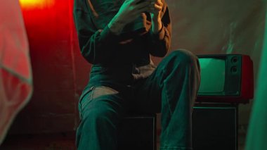 Bir kadın, loş ışıklı, antika bir odada retro televizyonla otururken akıllı telefonunu kullanmaya odaklanır. Yavaş çekim