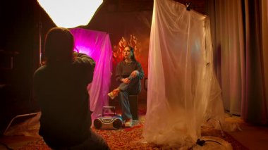 Sahne arkasında. Bir fotoğrafçı sanatsal arkaplanlar arasında canlı ışıklandırma ve aksesuar kullanarak yaratıcı bir portre yakalar..