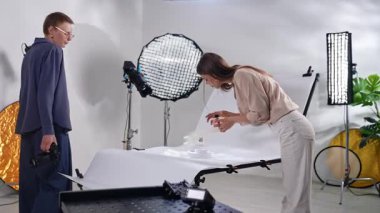 Sahne arkasında. İki yaratıcı profesyonel modern bir fotoğraf stüdyosunda, profesyonel ışıklandırma altında eşyalar düzenlemek ve fotoğraflamak için işbirliği yapıyorlar..