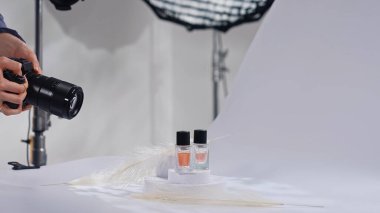 Sahne arkasında. Profesyonel bir fotoğrafçı, bir stüdyo ortamında, ışıklandırma ve kompozisyona odaklanmış parfümlerin sanatsal bir fotoğrafını çekiyor..