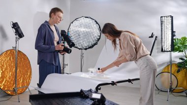 Sahne arkasında. İki yaratıcı profesyonel modern bir fotoğraf stüdyosunda, profesyonel ışıklandırma altında eşyalar düzenlemek ve fotoğraflamak için işbirliği yapıyorlar..