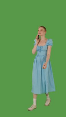 Mavi elbiseli bir insan, akıllı telefonla konuşurken parlak yeşil bir ekrana karşı yürüyor, kroma anahtarı. Yarım dönüş görünümü