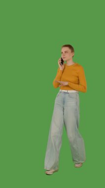 Sarı bluzlu ve kot pantolonlu biri akıllı telefonla konuşurken parlak yeşil ekran, krom anahtar karşısında yürür. Yarım dönüş görünümü