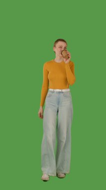 Yürürken, kulaklık takarken, kot pantolon giyerken ve turuncu bir kazak giyerken müziğin keyfini çıkaran bir insan, canlı yeşil bir arkaplan üzerine kuruludur..