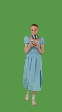 Yürümekten hoşlanan, kulaklık takan, kot mavisi elbise giyen, canlı yeşil ekran, krom anahtara dayanan bir kişi.