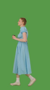 Mavi elbiseli, elinde kupa, yeşil ekranda yürüyen, krom anahtarı olan biri. Yan görünüm