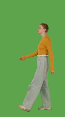 Sarı kazaklı ve geniş paçalı kotlu biri yeşil ekranda yürüyor, kroma anahtarlı. Yan görünüm, dikey video