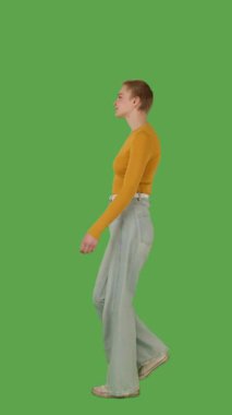 Sarı kazaklı ve geniş paçalı kotlu biri yeşil ekranda yürüyor, kroma anahtarlı. Yan görünüm, dikey video