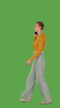 Sarı bluzlu ve kot pantolonlu biri akıllı telefonla konuşurken parlak yeşil ekran, krom anahtar karşısında yürür. Yan görünüm, dikey video