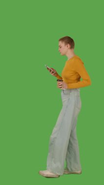 Bir insan yürür ve bir elinde akıllı telefon, diğer elinde bir bardak, yeşil ekranda ise krom anahtar kullanır. Yan görünüm, dikey video