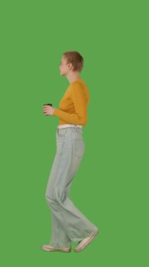 Sarı bluz giyen, elinde fincan tutan, yeşil ekranda yürüyen, krom anahtarı olan biri. Yan görünüm, dikey video