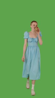 Mavi elbiseli, elinde kupa, yeşil ekranda yürüyen, krom anahtarı olan biri. Dikey video