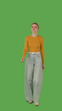 Sarı kazaklı ve geniş paçalı kotlu biri yeşil ekranda yürüyor, kroma anahtarlı. Dikey video