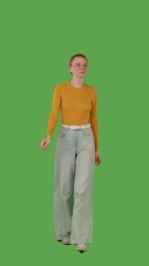 Sarı kazaklı ve geniş paçalı kotlu biri yeşil ekranda yürüyor, kroma anahtarlı. Dikey video