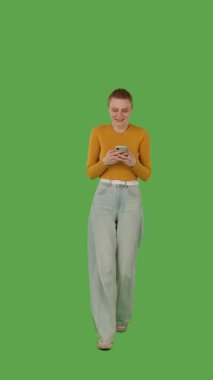 Sarı bluz ve kot pantolon giyen yeşil ekrana karşı akıllı telefonuna odaklanan biri, kroma anahtar. Dikey video