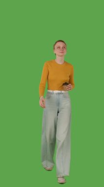Sarı bluz giyen, elinde fincan tutan, yeşil ekranda yürüyen, krom anahtarı olan biri. Dikey video