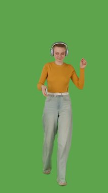 Yürüyerek, kulaklık takarak, kot pantolon giyerek ve turuncu bir kazak giyerek müziği seven bir insan, canlı yeşil bir arka planda yer alır. Dikey video