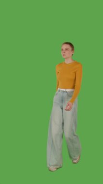 Sarı kazaklı ve geniş paçalı kotlu biri yeşil ekranda yürüyor, kroma anahtarlı. Yarım dönüş görünümü, dikey video