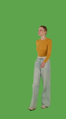 Sarı kazaklı ve geniş paçalı kotlu biri yeşil ekranda yürüyor, kroma anahtarlı. Yarım dönüş görünümü, dikey video