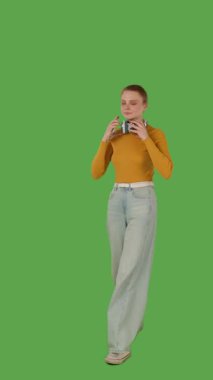 Yürümekten hoşlanan, kulaklık takan, kot pantolon giyen, turuncu kazak giyen, canlı yeşil ekran ve krom anahtarla çizilmiş bir insan. Yarım dönüş görünümü, dikey video