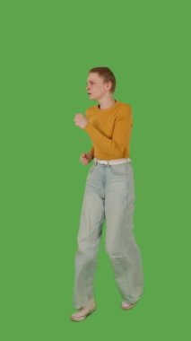 Sarı kazaklı ve geniş paçalı kotlu biri yeşil ekranda koşuyor, kroma anahtarı. Yarım dönüş görünümü, dikey video