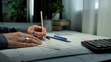 Taslak araçlarla çevrili, kalem ve cetvelle planlar üzerine mimari planlar çizen eller.