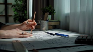 Eller, masa üzerine odaklanmayı ve beceriyi yansıtan kalem ve cetvel kullanarak ayrıntılı bir mimari plan çiziyor..