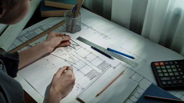 Tasarımda hassasiyeti vurgulayan, planlar, çizim araçları ve hesap makinesi gösteren bir mimarın çalışma alanı.