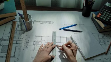 Bir mimar, cetvel ve kalemler de dahil olmak üzere çeşitli taslak araçlarıyla ayrıntılı bir plan üzerinde çalışır..