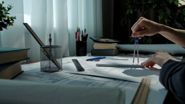 Pusula ve cetvel kullanan bir mimar çizim malzemeleriyle dolu bir masanın planlarında..