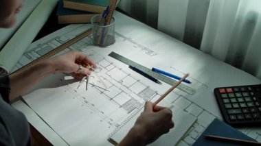 Tasarımda hassasiyeti vurgulayan, planlar, çizim araçları ve hesap makinesi gösteren bir mimarın çalışma alanı. Yavaş çekim