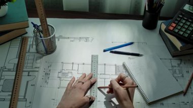 Bir mimar, cetvel ve kalemler de dahil olmak üzere çeşitli taslak araçlarıyla ayrıntılı bir plan üzerinde çalışıyor. Yavaş çekim