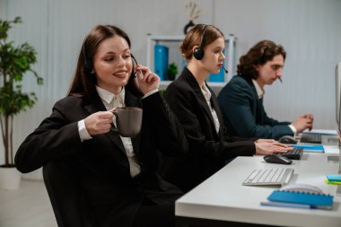 Bir grup müşteri hizmetleri temsilcisi kulaklık takıyor ve modern ofis ortamında bilgisayar başında çalışıyor..