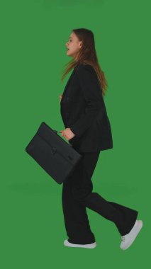 Elinde evrak çantası olan takım elbiseli bir iş kadını yeşil ekran, krom anahtara doğru emin adımlarla yürüyor. Yan görünüm