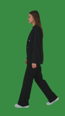 Zarif siyah takım elbiseli ve beyaz spor ayakkabılı bir kadın yeşil ekrana, krom anahtara güvenerek yürür. Yan görünüm