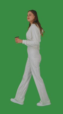 Beyaz elbiseli genç bir kadın, kahvesini yeşil ekran ve krom anahtarla içiyor. Yan görünüm