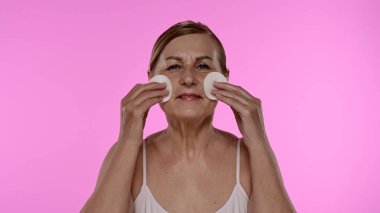 Üst düzey bir kadın yüzünü pamuk pedlerle nazikçe temizliyor, cilt bakımına ve sağlığına odaklanıyor..