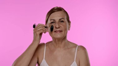 Gecelikli bir kadın yüz silindiri kullanıyor. Bu araç cilt esnekliğini arttırır ve şişkinliği azaltır.