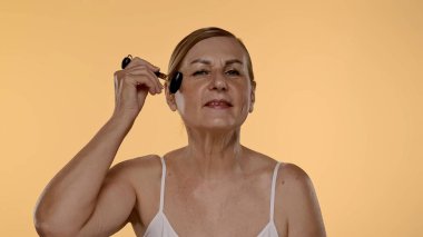 Gecelikli bir kadın yüz silindiri kullanıyor. Bu araç cilt esnekliğini arttırır ve şişkinliği azaltır.