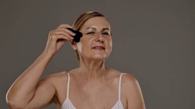 Yaşlı bir kadın yüz masajı için gua sha aracı kullanır, cilt bakımı, rahatlama ve gençleştirme teknikleri gösterir.