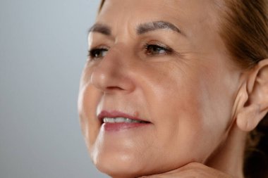 Olgun bir kadının düşünceli yüz ifadesini yaklaştır. Elleri nazikçe yüzünde dinleniyor..